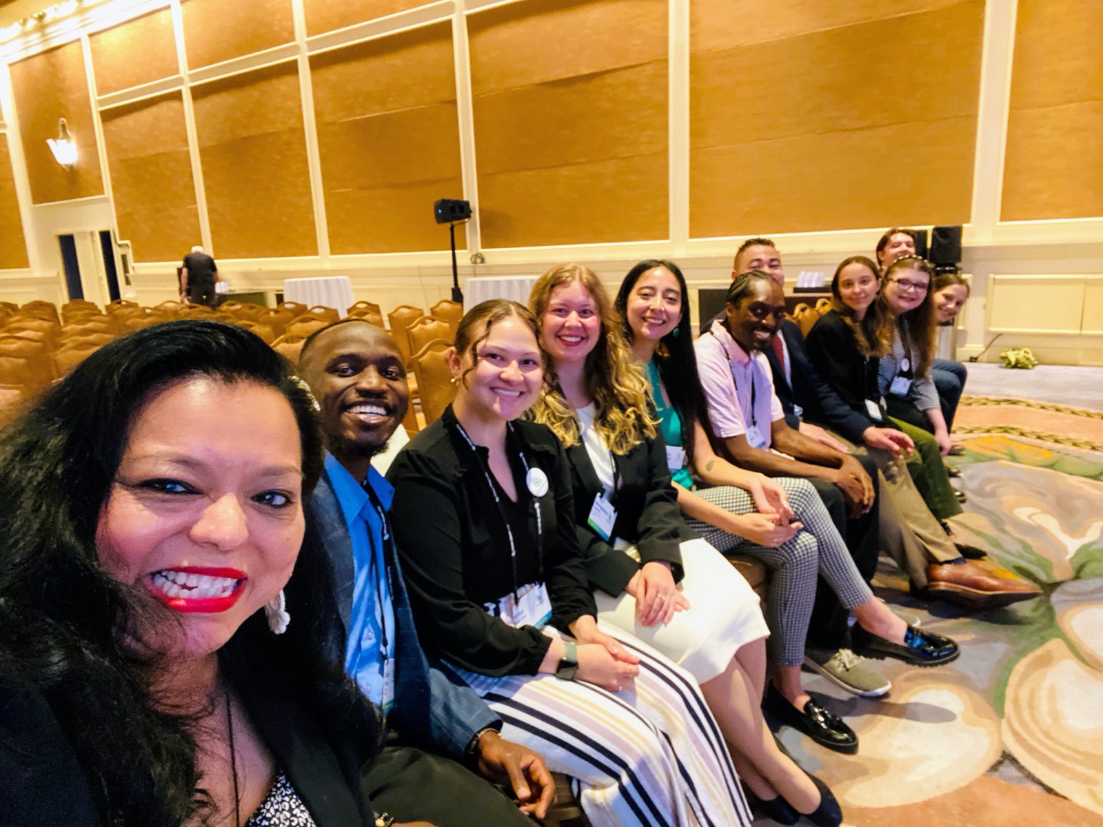 A row of smiling PGM members taking a selfie in a conference hall