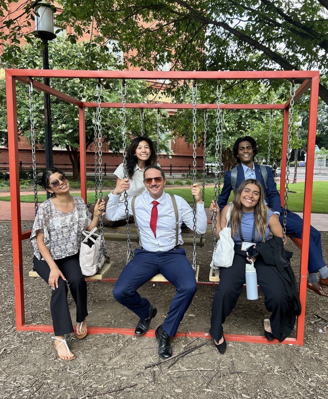 Five PGM volunteers laughing together on a playground swing set