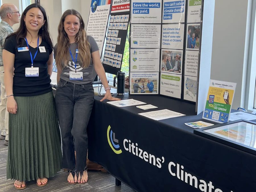 Two volunteers beside a Citizens&rsquo; Climate outreach display at a tabling event