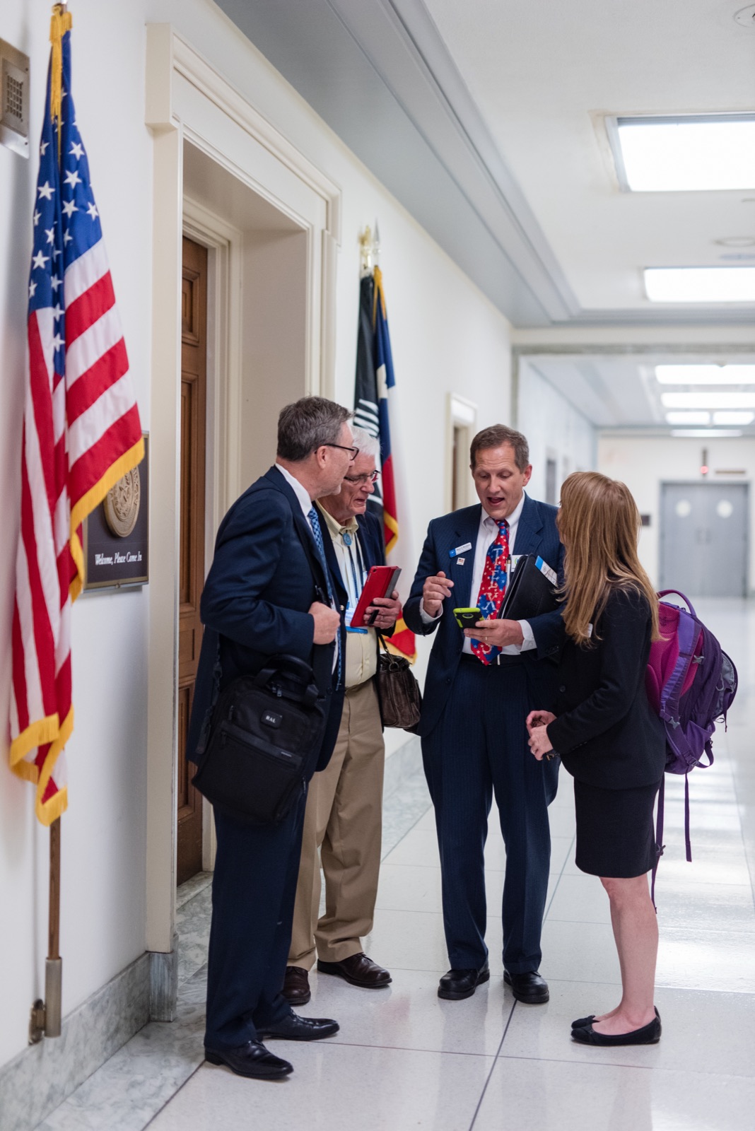 Four CCL volunteers share a laugh outside a congressional office, an American flag beside them