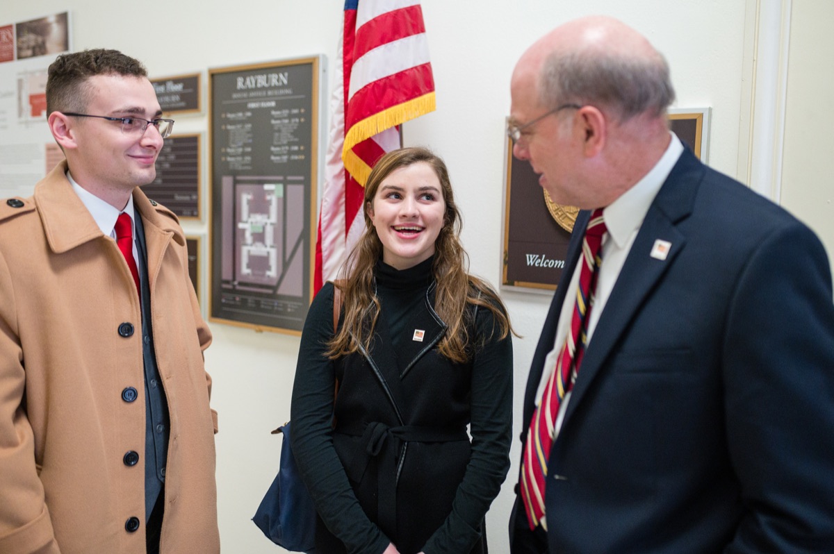 Two young CCL volunteers in conversation with an older advocate beside an American flag in the Rayburn building
