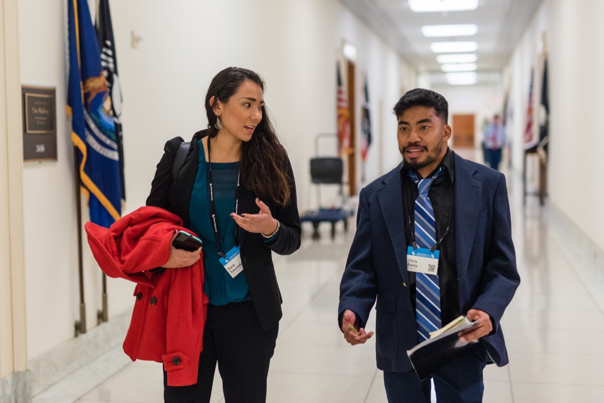 Two volunteers walk a congressional hallway lined with flags
