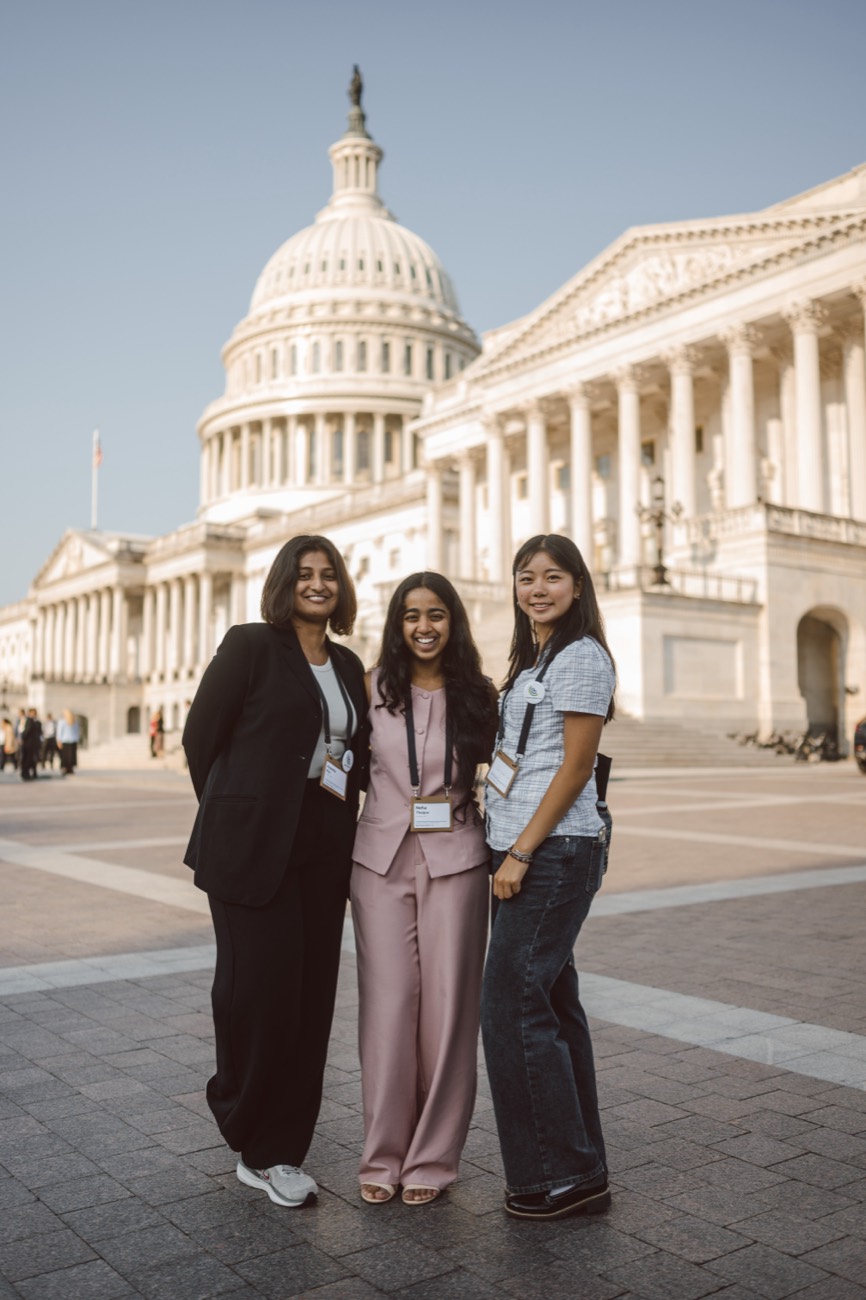 Three young women volunteers in front of the Capitol dome